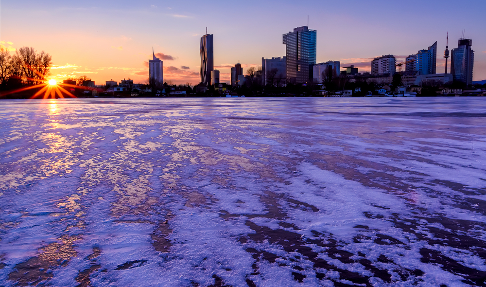 Die zugefrorene Alte Donau in Wien mit den Hochhäusern und der untergehenden Sonne im Hintergrund