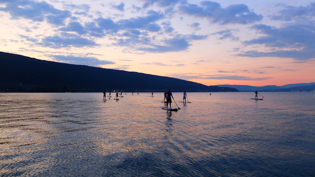 Einige Standup-Paddler auf einem großen See mit Sonnenuntergang (c) flickr / Benoit Mouren