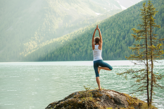 Junge Frau steht in Yogapose vor einem See (c) My Good Images / shutterstock