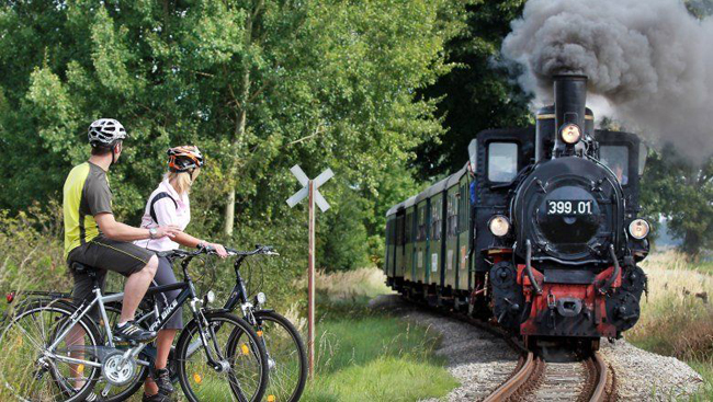 Eine Dampflokomotive der Waldviertelbahn sowie zwei Personen auf Fahrrädern. © NOEVOG/weinfranz.at